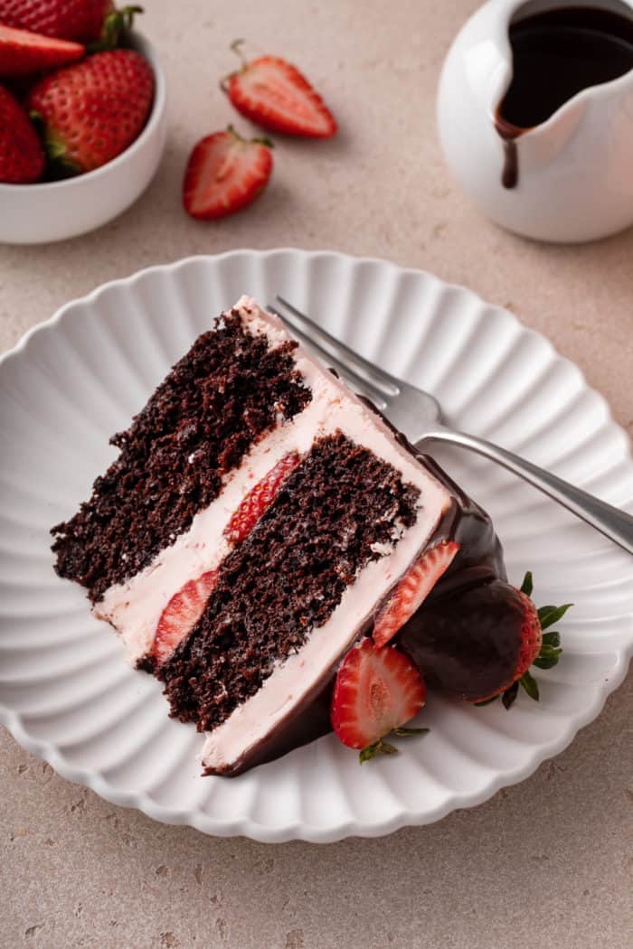 Slice of chocolate strawberry cake next to a fork on a white plate.