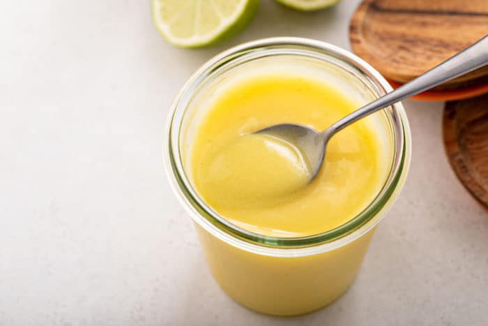 Jar filled with lime curd with a spoon resting on the top of the jar.