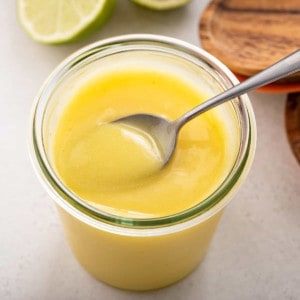 Spoon of lime curd resting on top of a jar of lime curd.