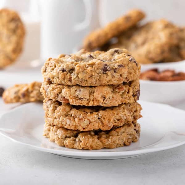 Four cowboy cookies stacked on a white plate.