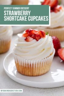 Strawberry shortcake cupcake topped with whipped cream frosting and diced strawberries set on a white plate. Text overlay includes recipe name.