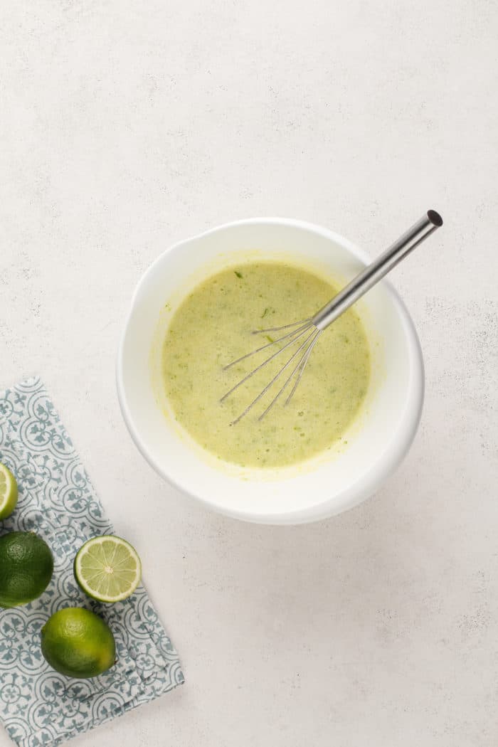 Ingredients for lime curd whisked together in a white mixing bowl, ready to be cooked in the microwave.