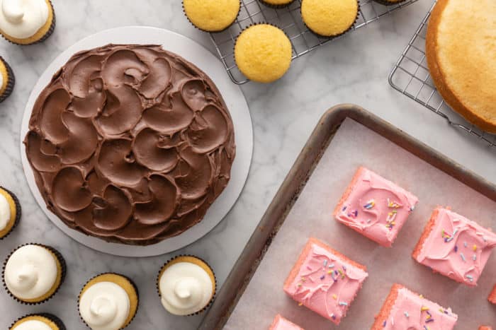 Assortment of frosted and unfrosted cakes on a marble countertop for freezing.