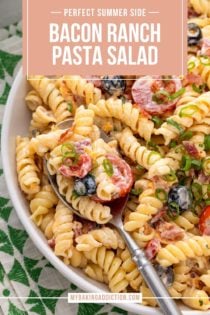 Close up of bacon ranch pasta salad in a white bowl. A silver serving spoon is also in the bowl. Text overlay includes recipe name.