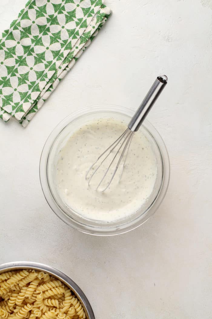Ranch dressing for pasta salad being whisked together in a glass mixing bowl.