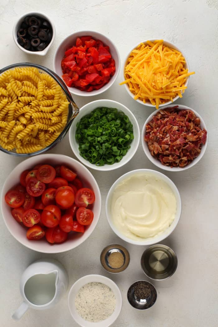 Ingredients for bacon ranch pasta salad arranged on a white countertop.