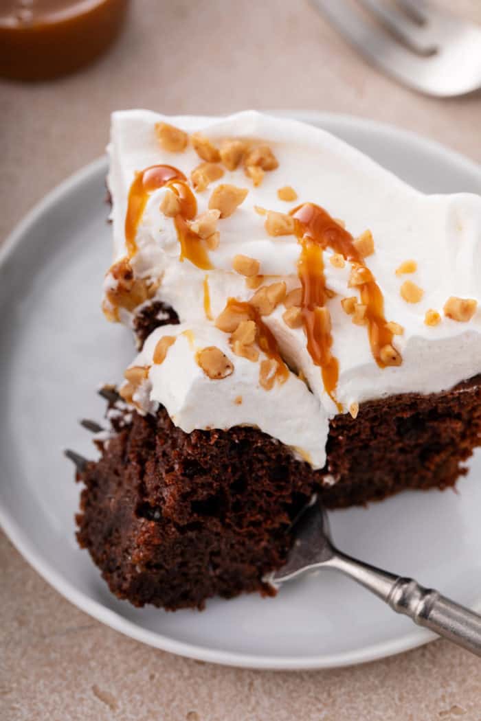 Fork cutting a bite off the corner of a slice of chocolate toffee poke cake.