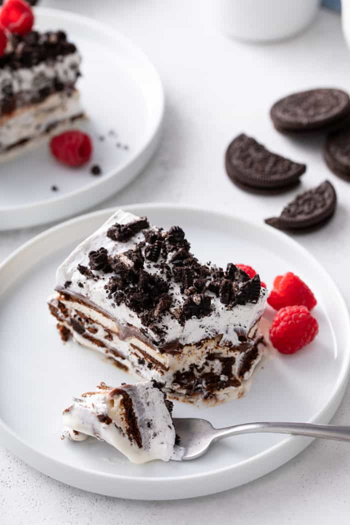 Fork with a bite of ice cream sandwich cake set onto a white plate next to a slice of ice cream sandwich plate.