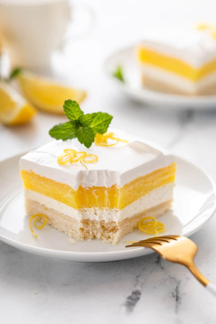 Bite taken from the corner of a slice of layered lemon dessert on a white plate.