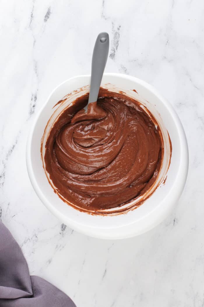 Chocolate cake batter being stirred in a white mixing bowl.