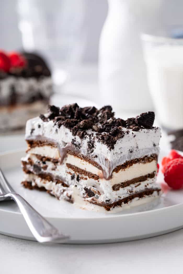 Close  up view of a slice of ice cream sandwich cake next to a fork on a white plate.