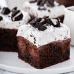 Close up slice of oreo poke cake on a white plate.