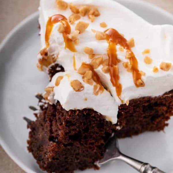 Fork cutting a bite off the corner of a slice of chocolate toffee poke cake.