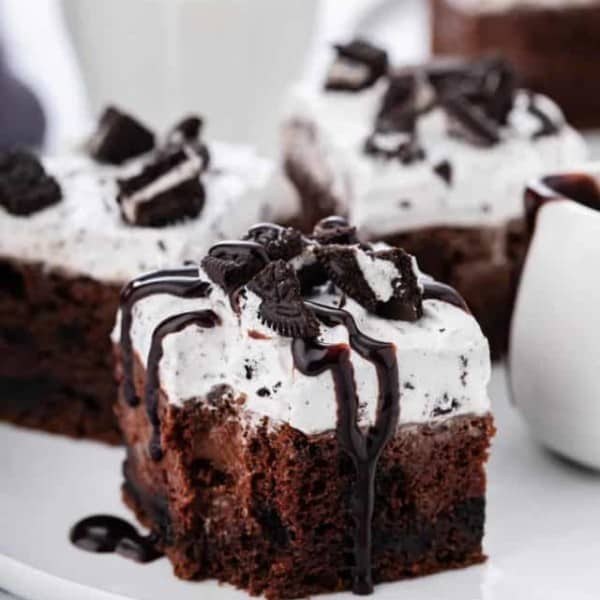 Slice of oreo poke cake drizzled with chocolate sauce, with a bite taken from the corner of the cake.
