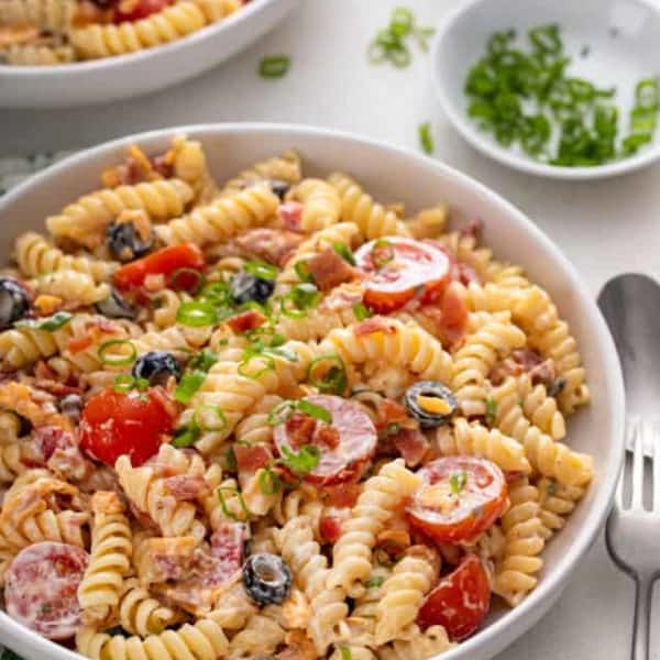 White bowl filled with bacon ranch pasta salad on a white countertop, with a second bowl visible in the background.