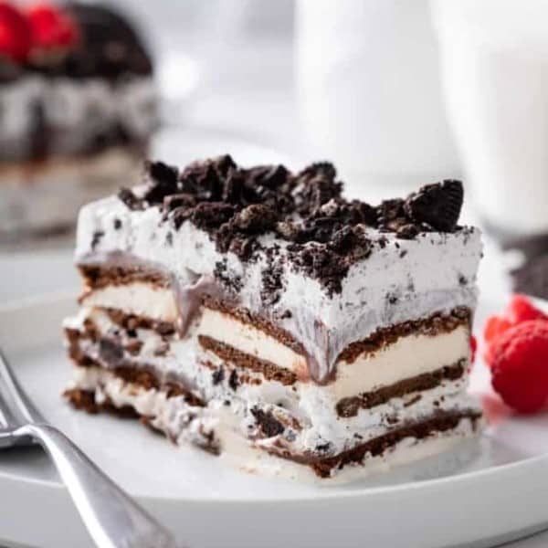Close up view of a slice of ice cream sandwich cake next to a fork on a white plate.