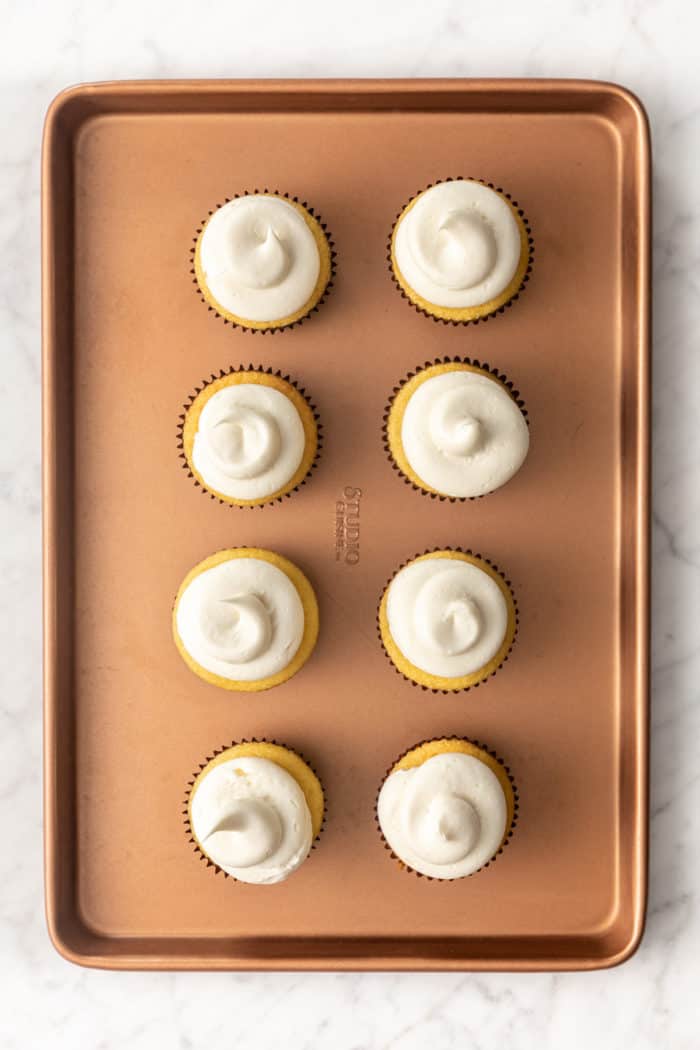 Eight frosted cupcakes set on a sheet tray, ready to go in the freezer.