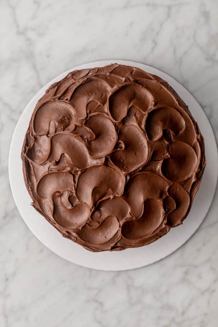 Whole, frosted chocolate cake on a cardboard cake round.