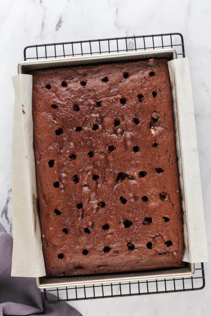 Chocolate oreo cake in a parchment-lined cake pan. The top of the cake has holes poked in it.