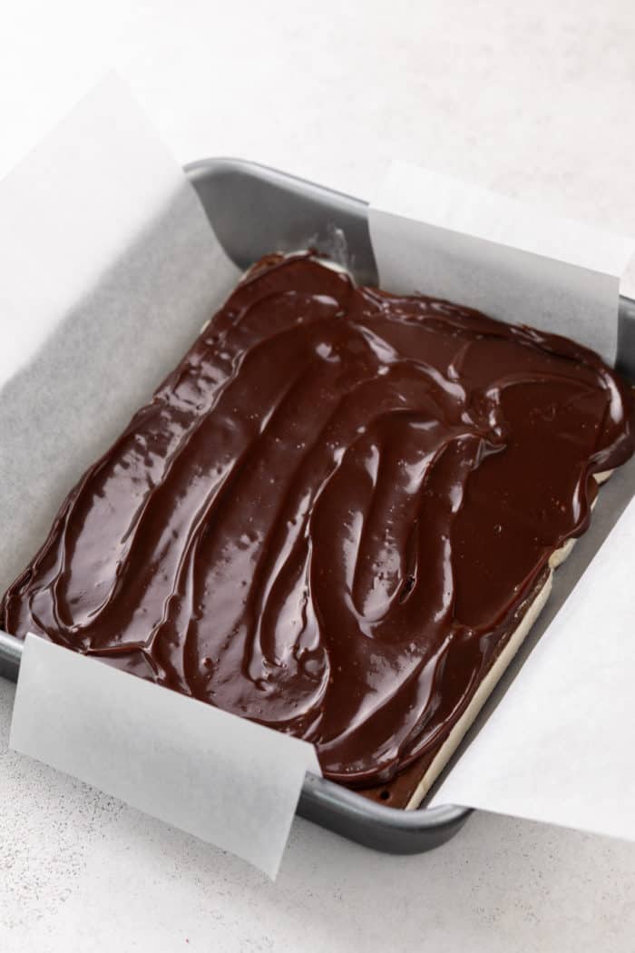 Hot fudge sauce spread on top of ice cream sandwiches in a square cake pan.
