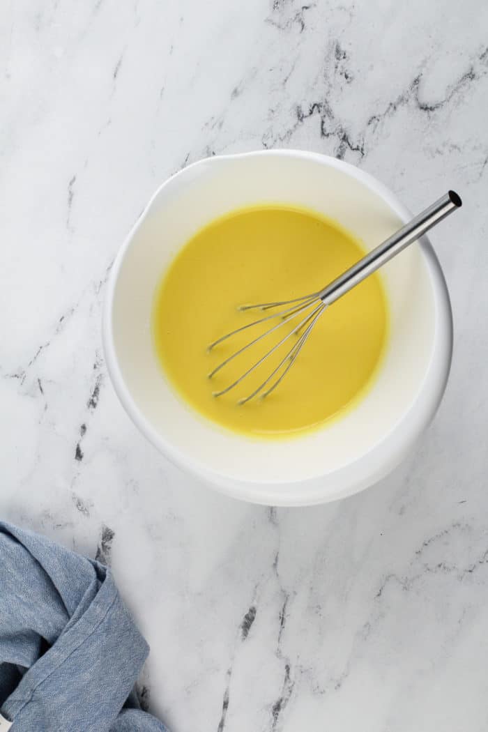 Lemon pudding being whisked together in a white mixing bowl for layered lemon dessert.