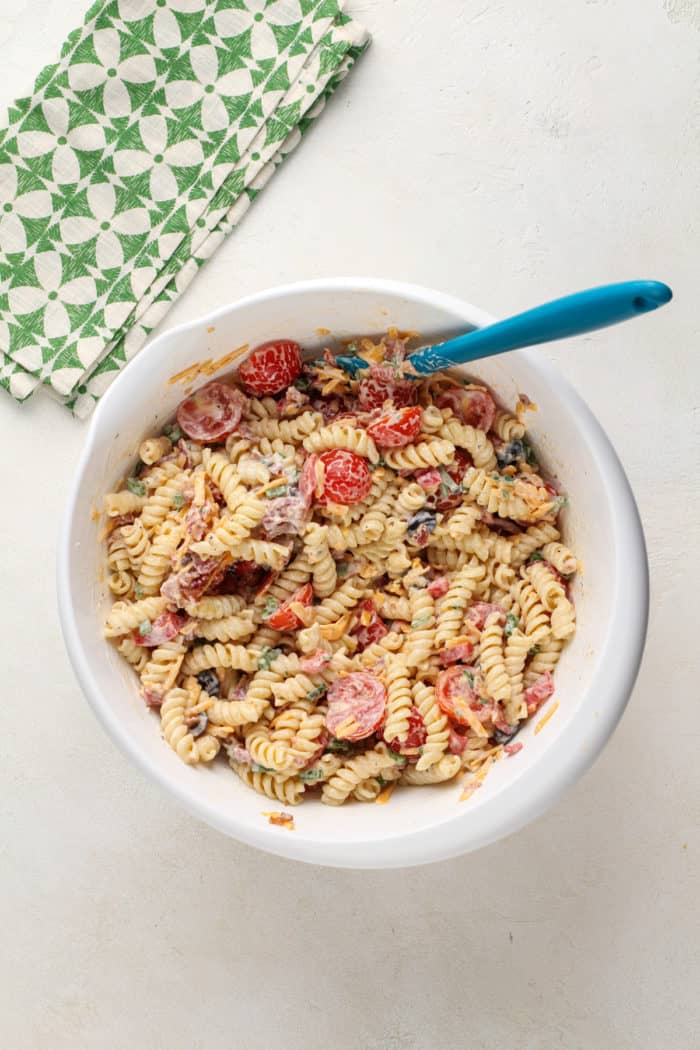 Bacon ranch pasta salad being mixed with a spatula in a white mixing bowl.