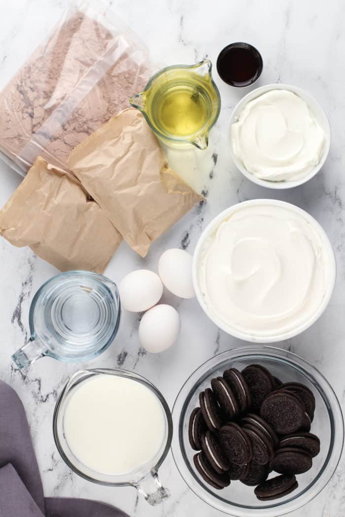 Ingredients for oreo poke cake arranged on a marble countertop.