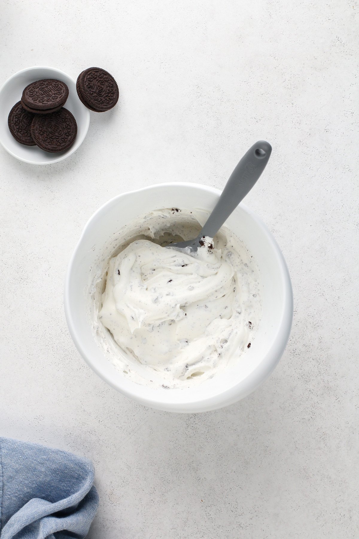 Chopped oreos folded into whipped topping in a white mixing bowl.