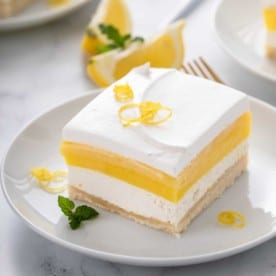 Close up image of a slice of layered lemon dessert on a white plate.