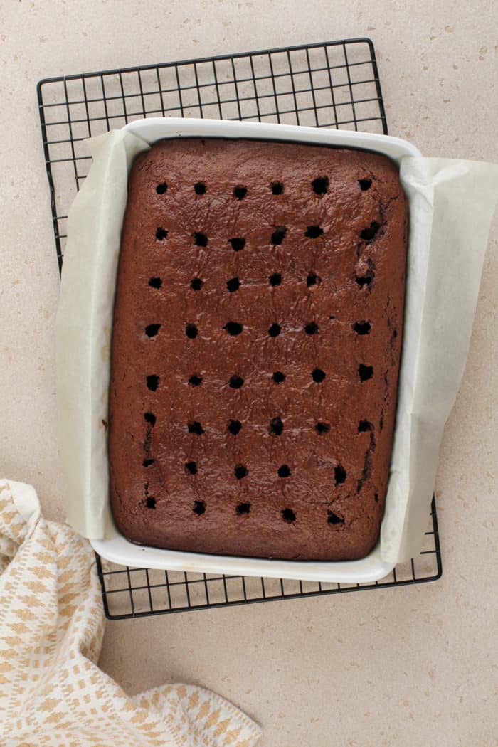 Chocolate cake in a white cake pan. The cake has holes poked across the top.