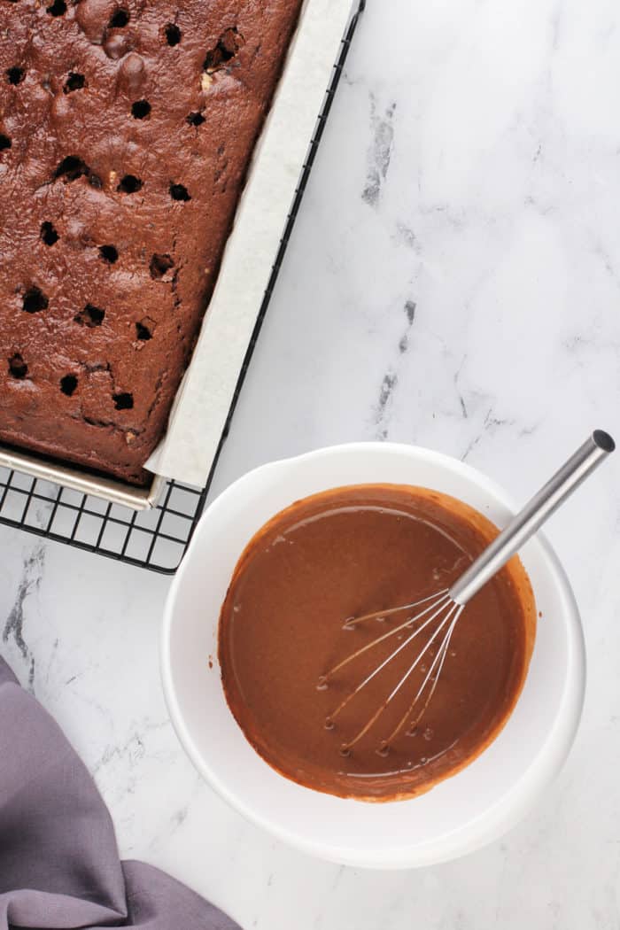 White bowl of chocolate pudding next to a chocolate cake with holes poked in it.