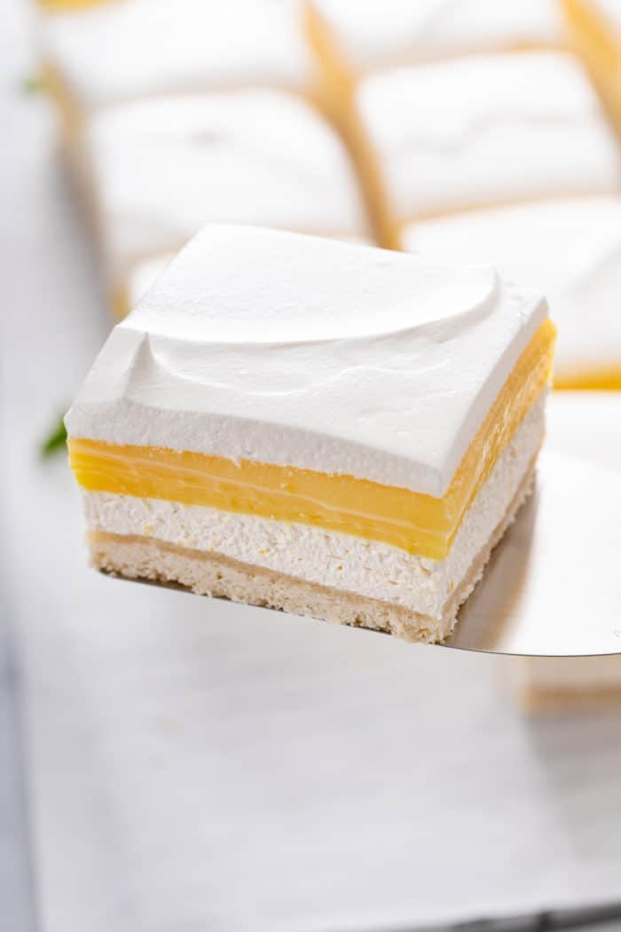 Cake server holding up a slice of layered lemon dessert, with more slices visible in the background.
