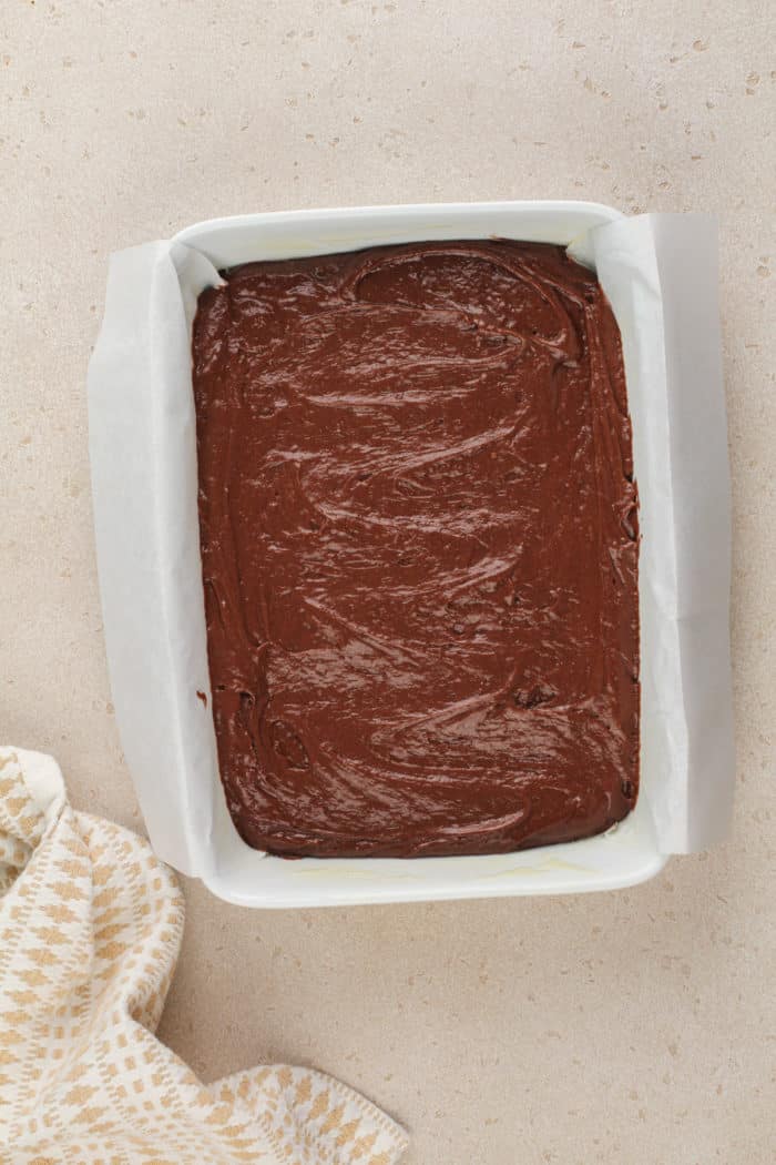 Batter for chocolate cake in a parchment-lined cake pan, ready to go in the oven.