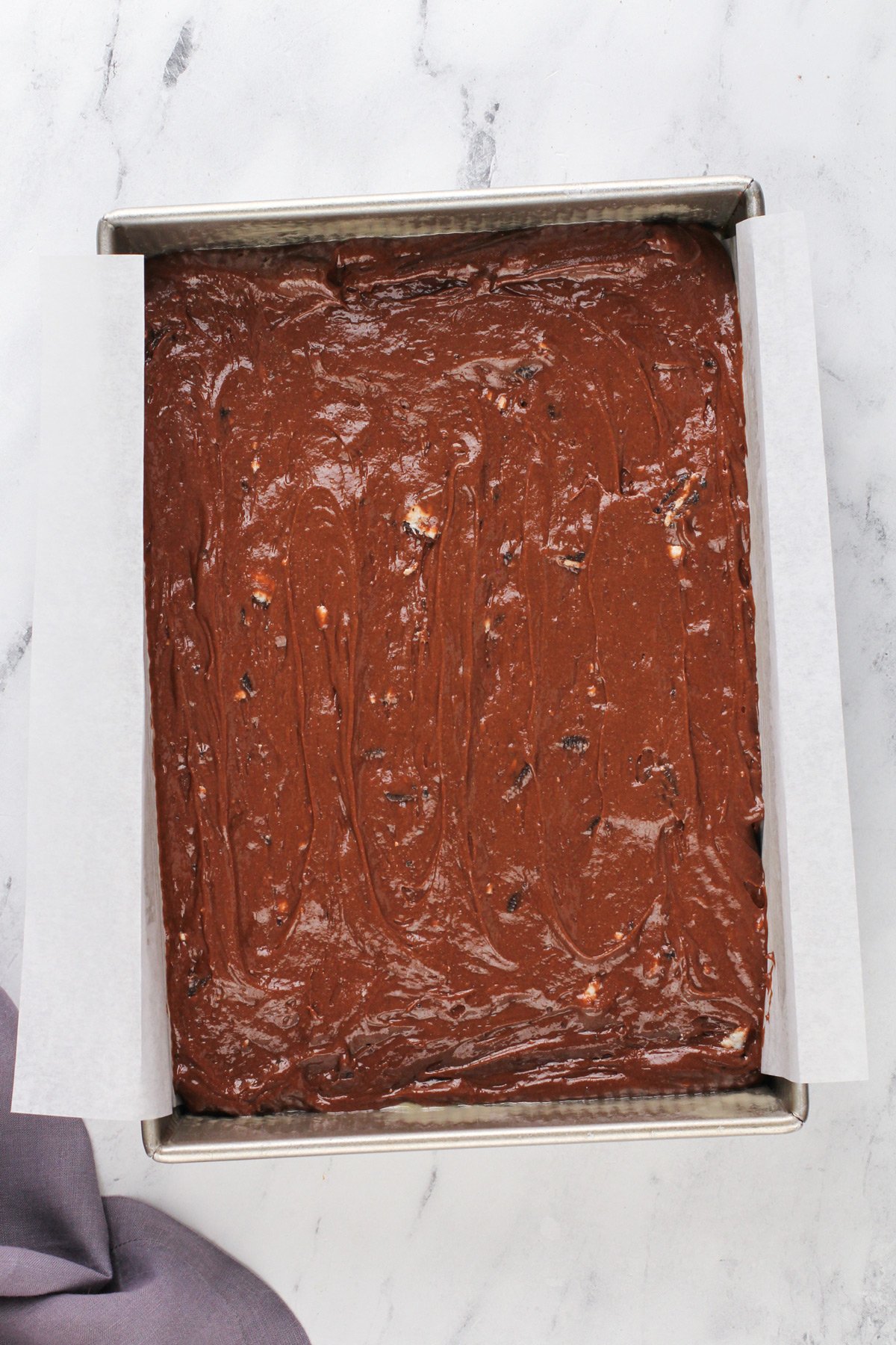 Chocolate cake batter with oreo pieces mixed into it spread into the bottom of a cake pan.