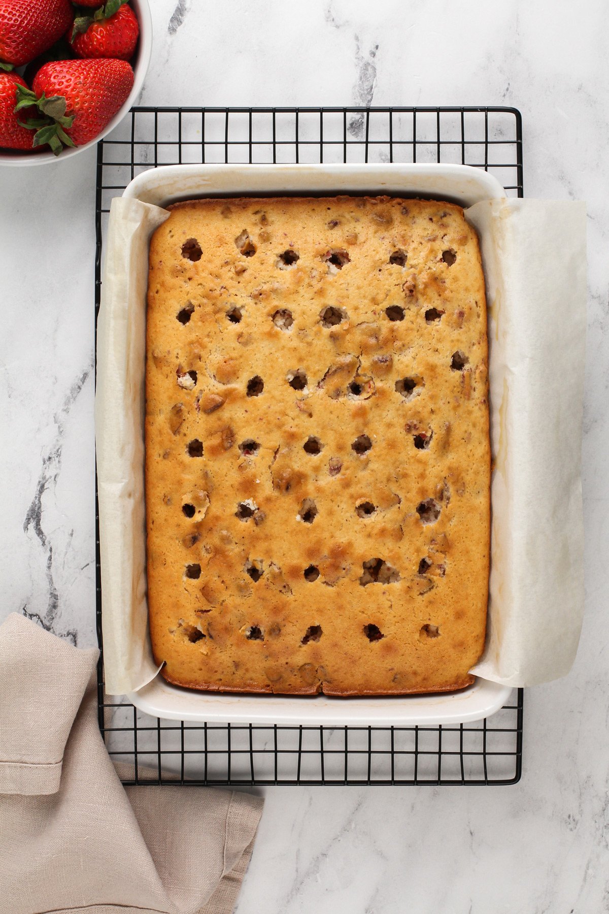 White cake with strawberries in it, baked in a cake pan with holes poked across the top of the cake.