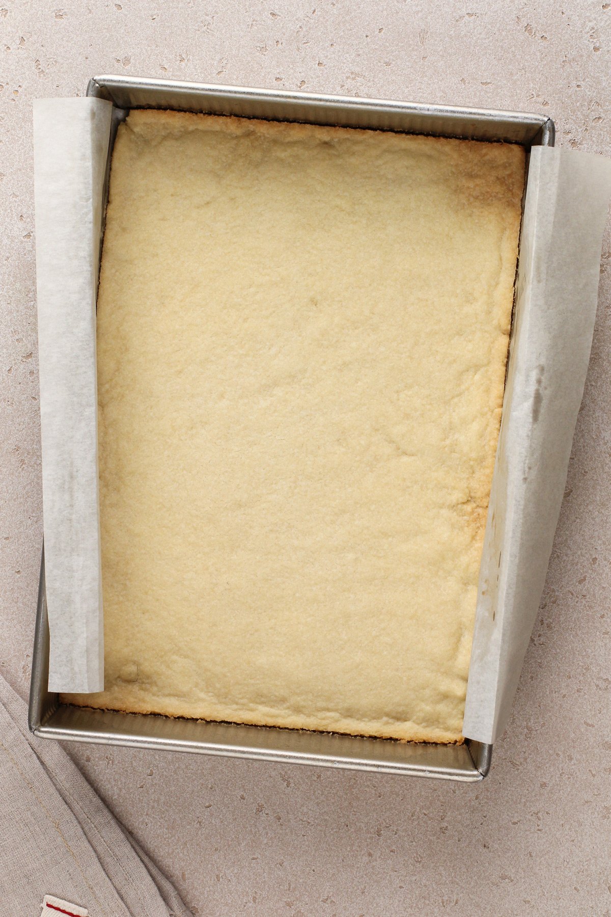Baked crust for layered cherry cheesecake dessert in the bottom of a parchment-lined baking pan.