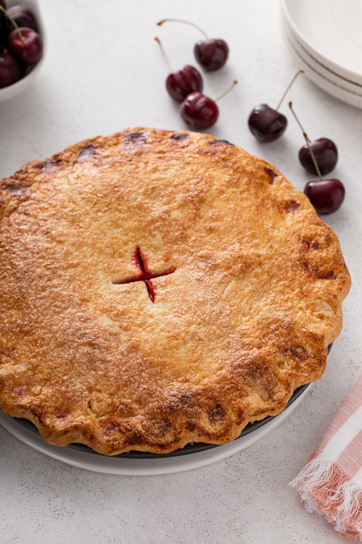 Baked cherry pie set on a light countertop next to fresh sweet cherries.