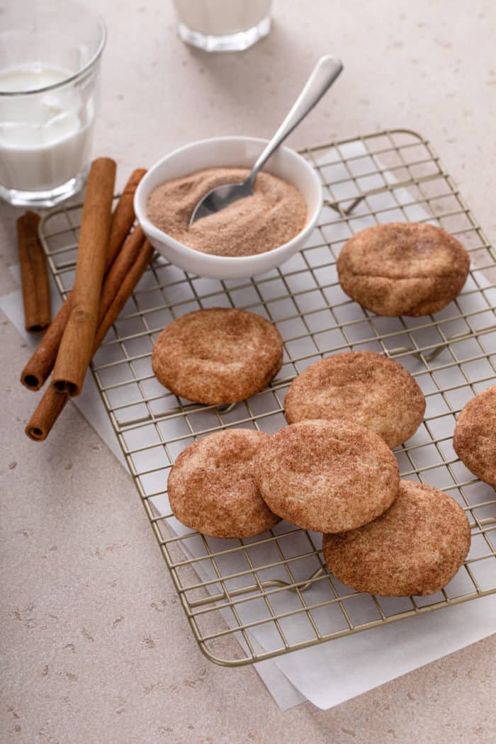 Snickerdoodles next to a bowl of cinnamon sugar on a wire cooling rack.