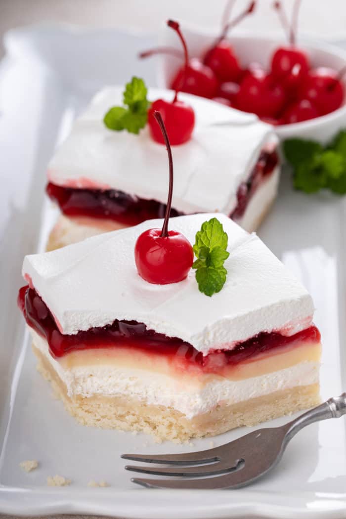 Slice of cherry cheesecake dessert on a white platter with a bite taken from it. A second slice is visible in the background.