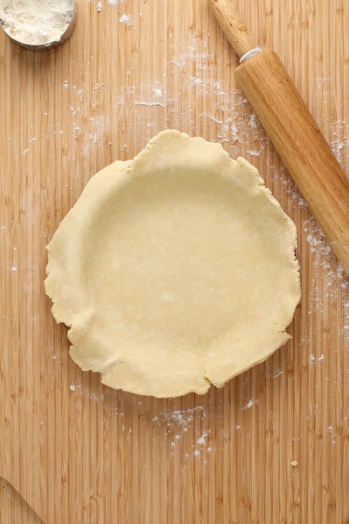 Pie crust nestled into a pie plate on a wooden board.