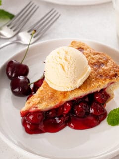 Slice of ice-cream-topped cherry pie on a white plate.