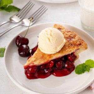 Slice of ice-cream-topped cherry pie on a white plate.