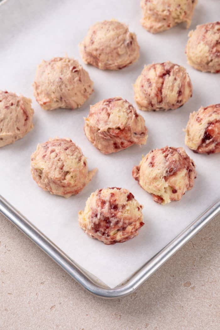 Balls of raspberry lemon cookie dough on a parchment-lined baking sheet, ready to chill in the refrigerator.