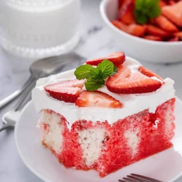 Slice of strawberry poke cake on a white plate. A bite has been taken from the corner of the cake.