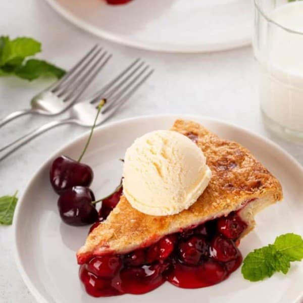 White plate with a slice of cherry pie topped with a scoop of vanilla ice cream.