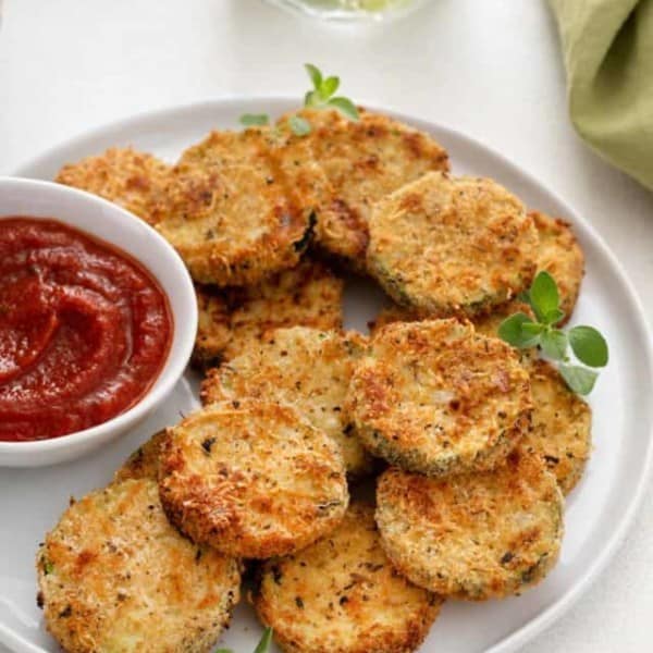 White plate filled with air fryer zucchini chips and a small bowl of marinara sauce.