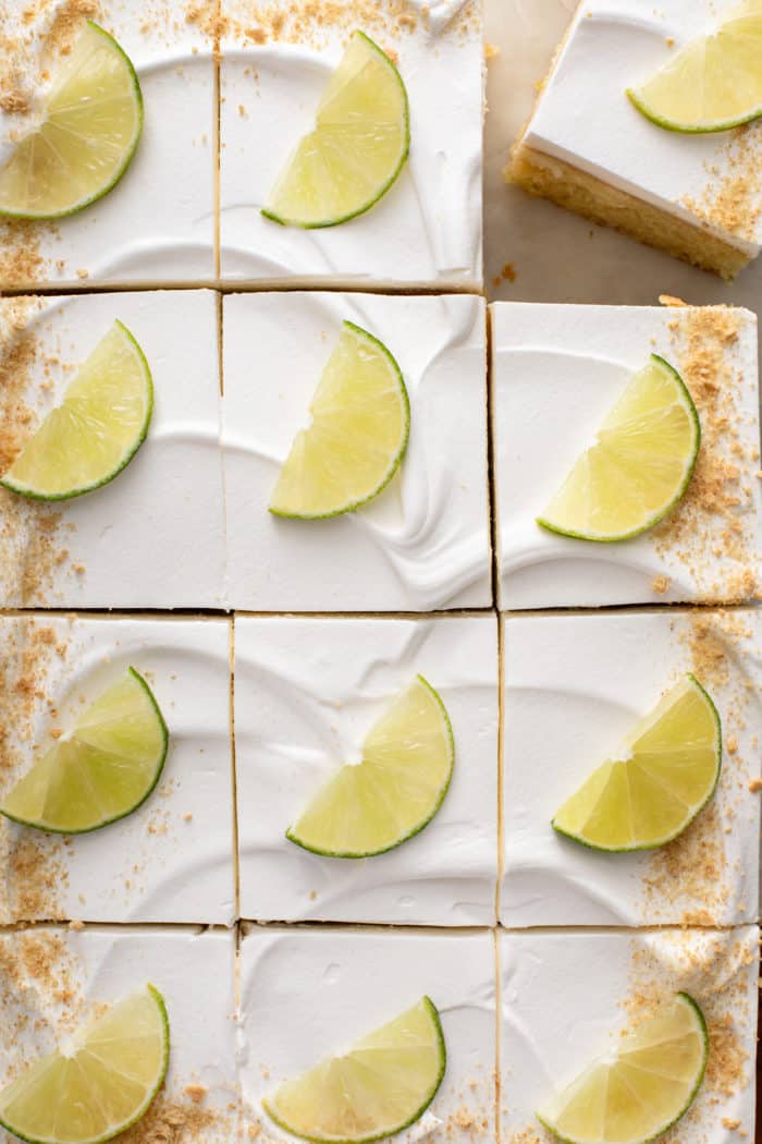 Overhead view of a sliced key lime poke cake garnished with graham cracker crumbs and slices of lime.
