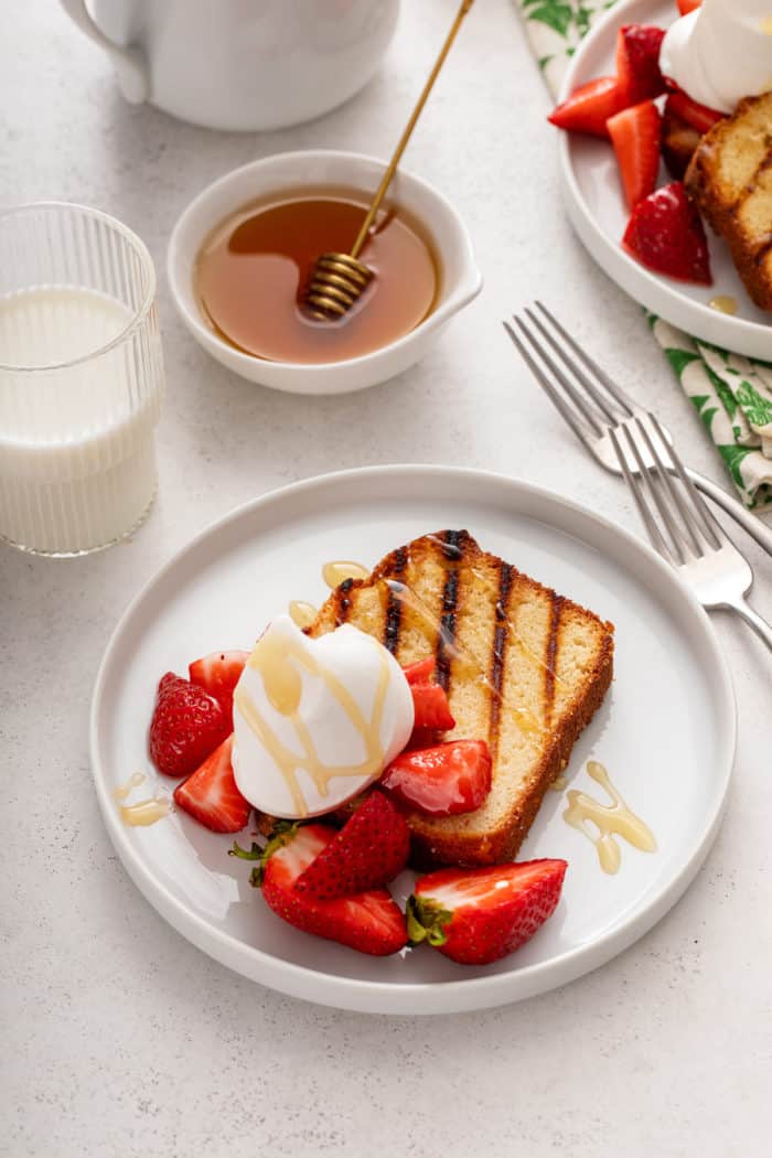 Slice of grilled pound cake topped with fresh strawberries, whipped cream, and a drizzle of honey.