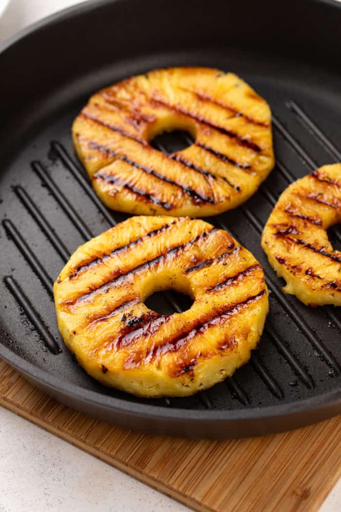 Three slices of pineapple being cooked on a grill pan.