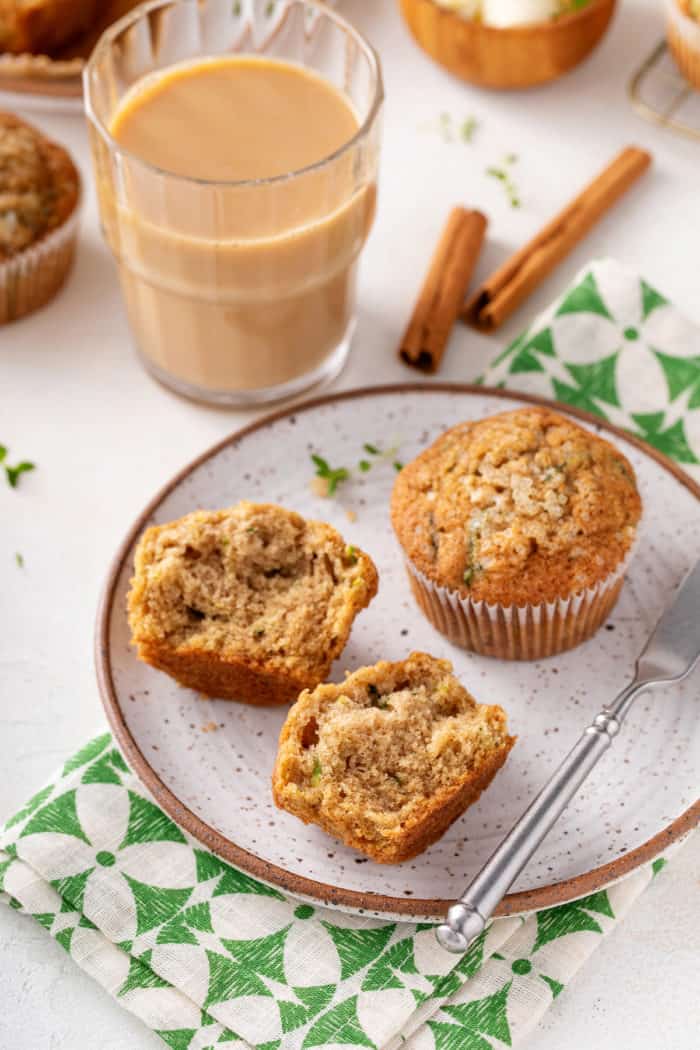 Two zucchini muffins on a stoneware plate. One muffin is whole and the other has been cut in half.